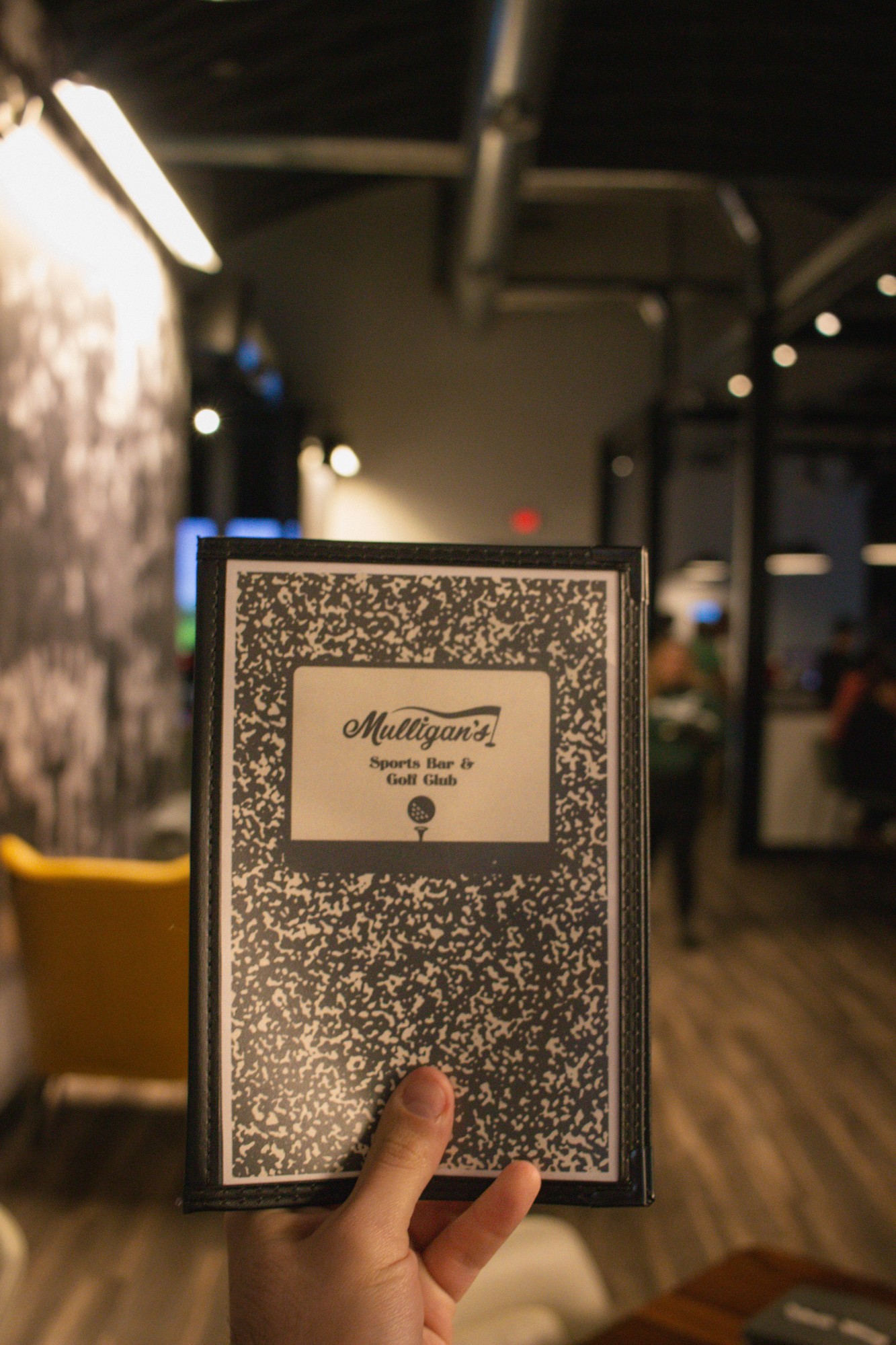 Hand holding black and white marble composition notebook drink menu inside Mulligan's lounge